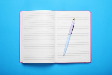 Photo of Open notebook and pen on light blue background, top view