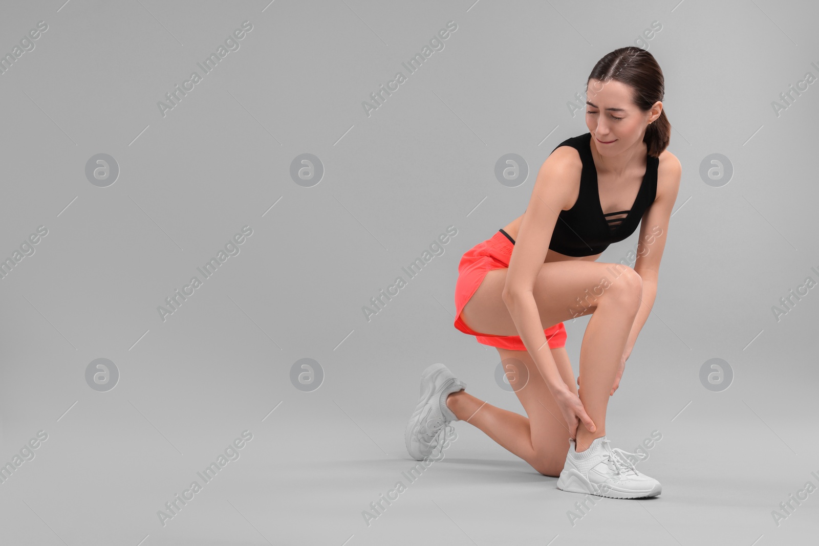 Photo of Young woman suffering from leg pain on grey background, space for text