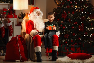 Photo of Merry Christmas. Surprised little boy receiving gift from Santa Claus at home