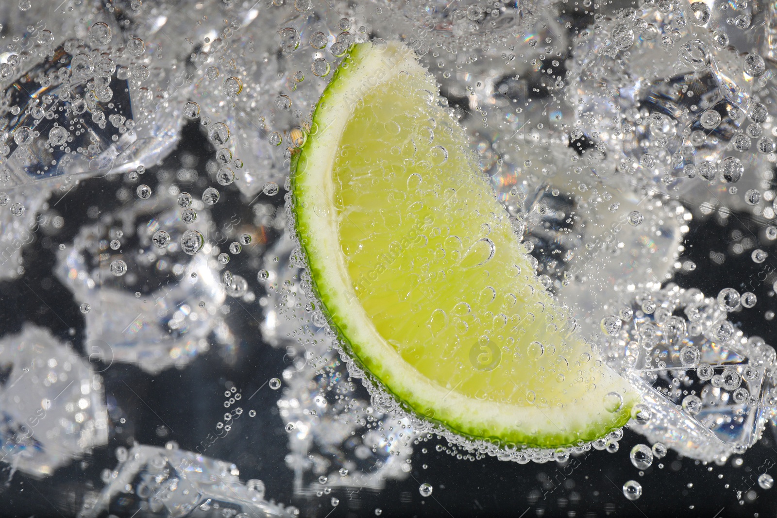 Photo of Juicy lime slice and ice cubes in soda water against black background, closeup