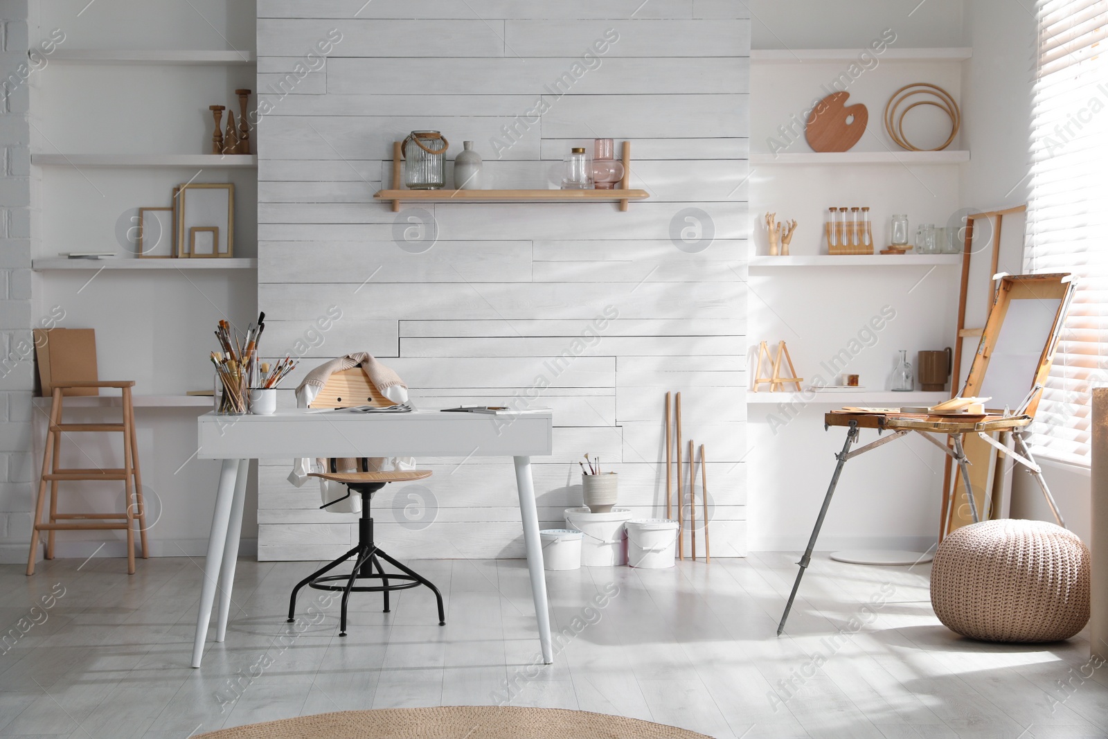 Photo of Modern studio interior with artist's workplace and wooden easel near large window