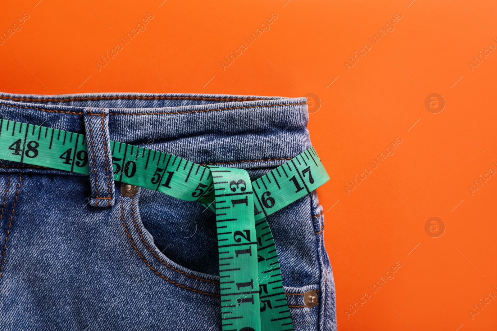 Photo of Jeans and measuring tape on orange background, top view. Weight loss concept