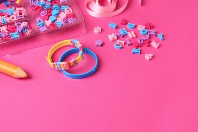 Photo of Handmade jewelry kit for kids. Colorful beads, ribbon and bracelets on bright pink background. Space for text