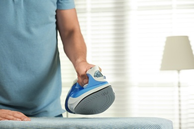 Photo of Handsome man ironing clean laundry at home, closeup