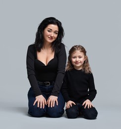 Photo of Beautiful mother with little daughter sitting on grey background