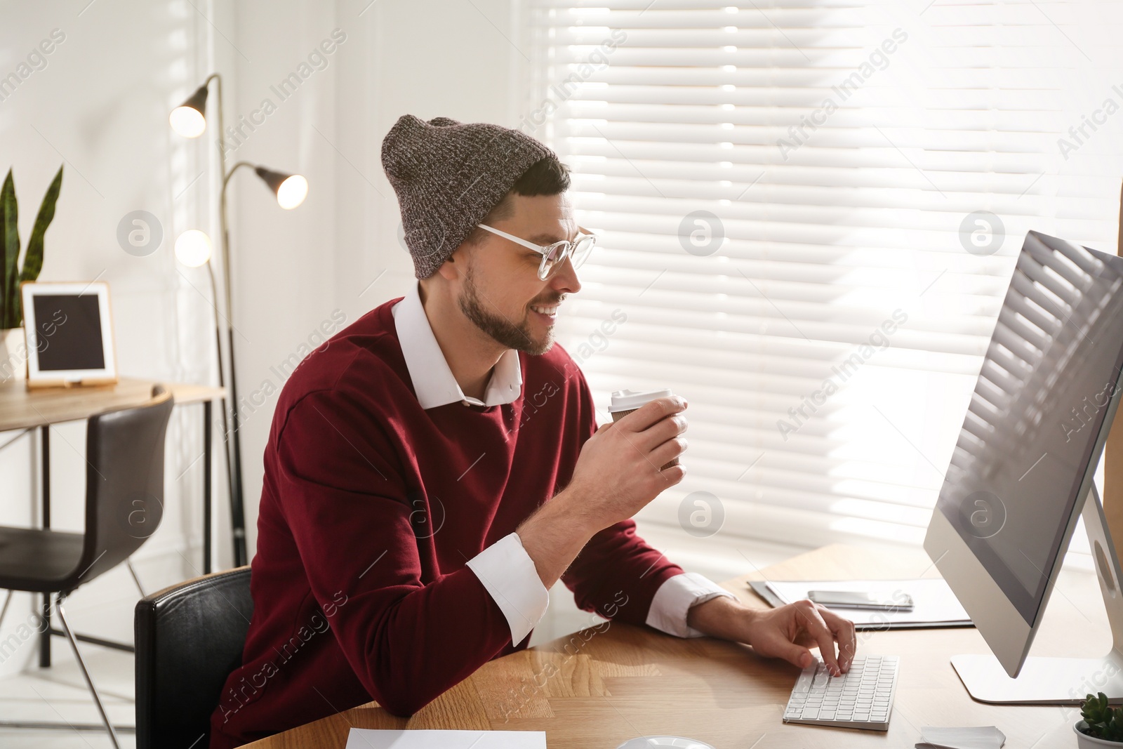 Photo of Freelancer with cup of coffee working on computer at table indoors