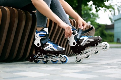 Photo of Woman wearing modern inline roller skates in city park, closeup