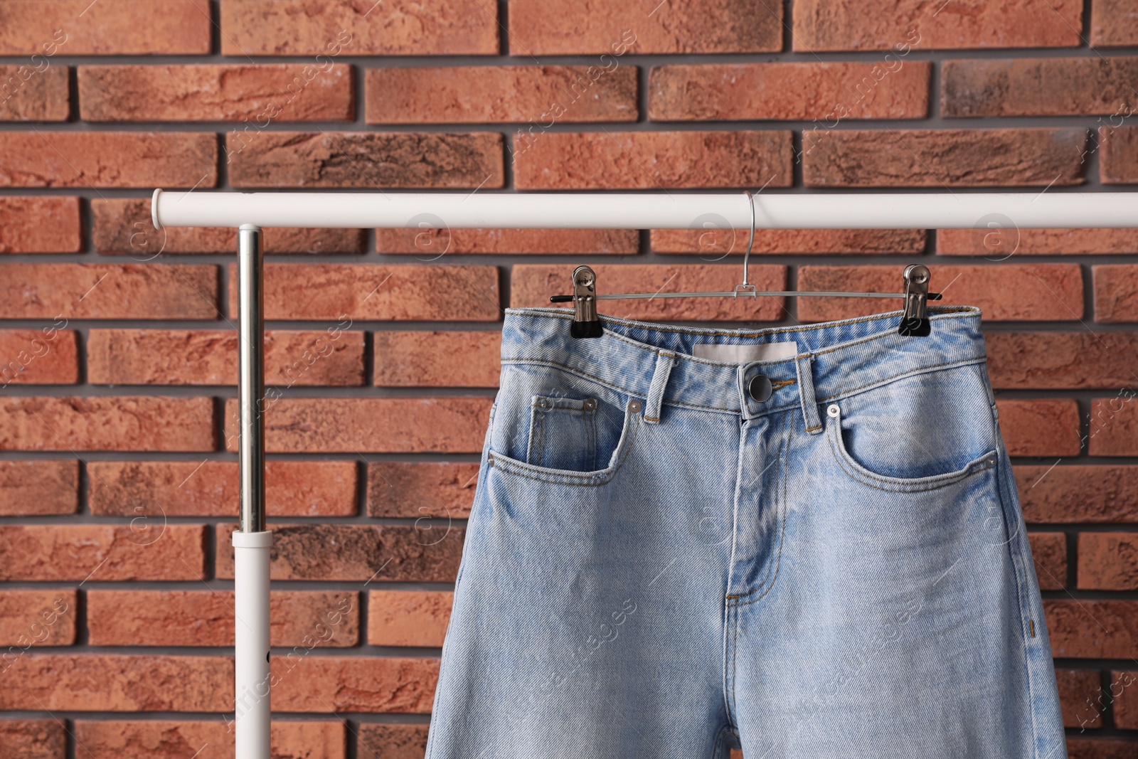 Photo of Rack with stylish jeans near brick wall, closeup