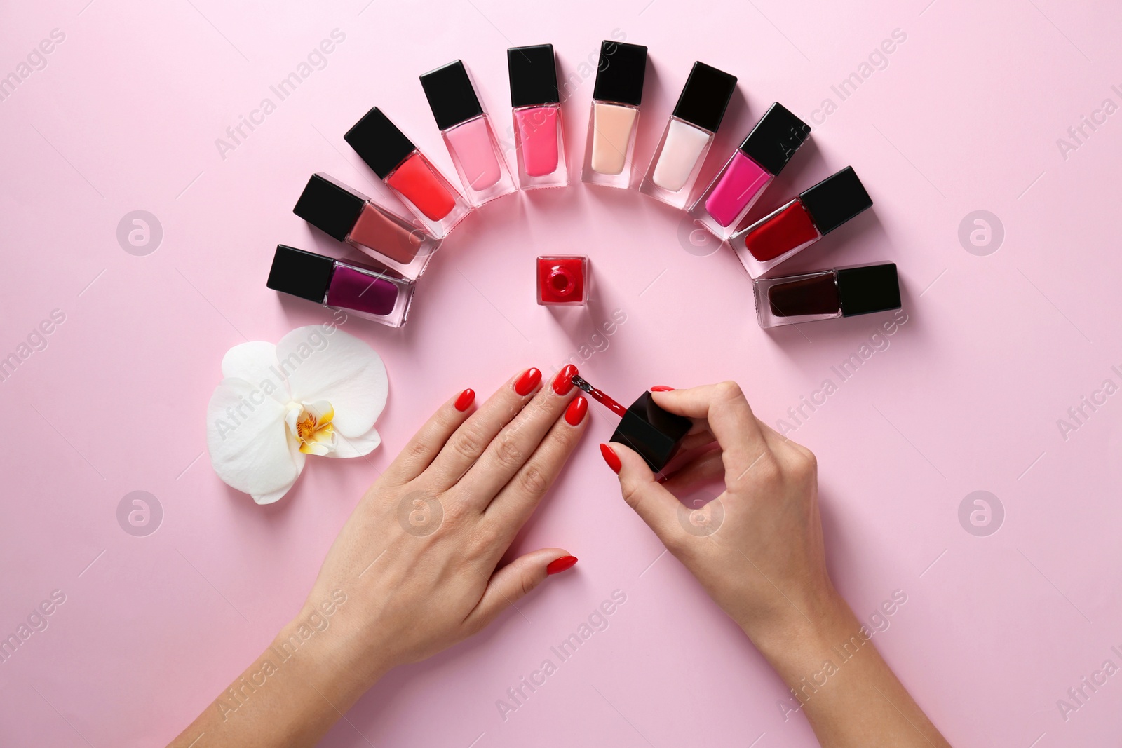 Photo of Woman applying bright nail polish on color background, top view