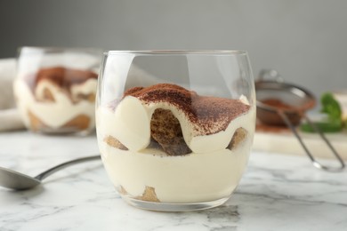 Photo of Delicious tiramisu in glass and spoon on white marble table, closeup