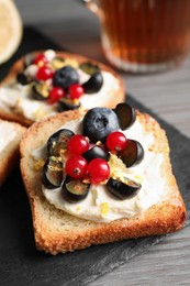 Photo of Tasty sandwiches with cream cheese, blueberries, red currants and lemon zest on slate plate, closeup