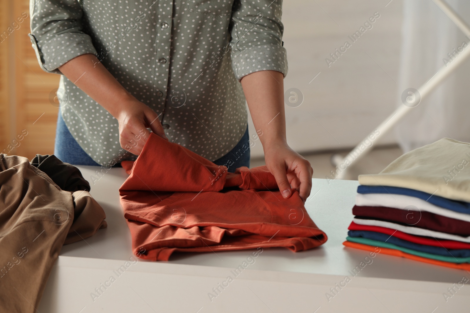 Photo of Woman folding clothes at white table indoors, closeup