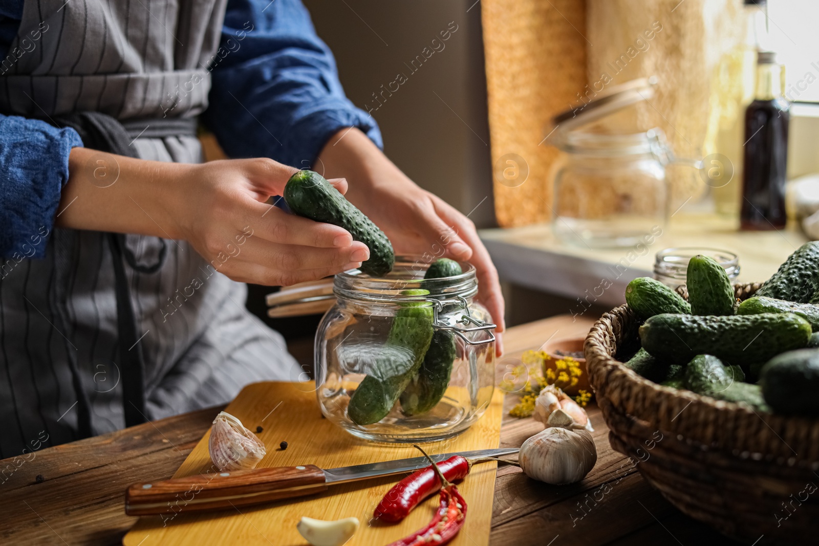 Photo of Woman putting cucumbers into jar at wooden table, closeup. Pickling vegetables