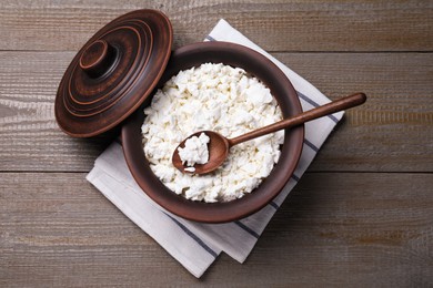 Photo of Top view of clay pot with cottage cheese and spoon on grey wooden table