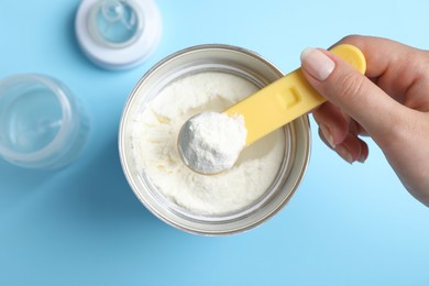 Photo of Woman taking powdered infant formula with scoop from can on light blue background, top view