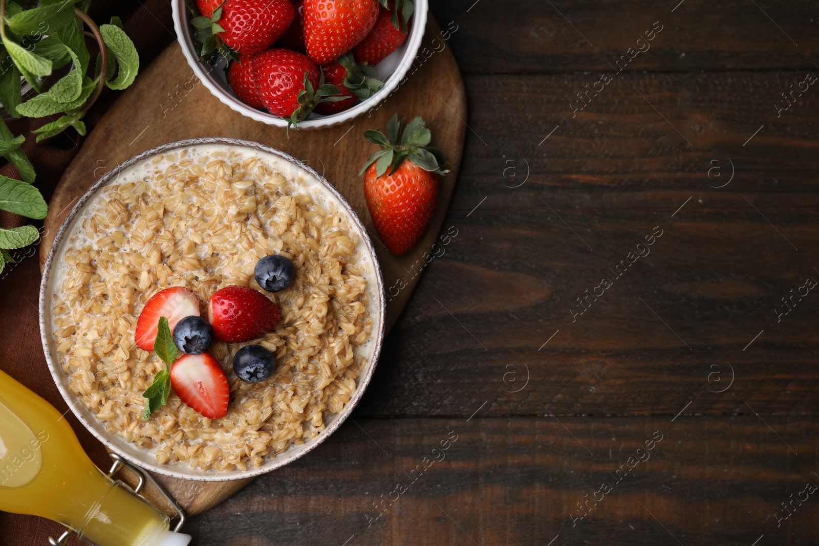 Photo of Tasty oatmeal with strawberries and blueberries in bowl on wooden table, flat lay. Space for text