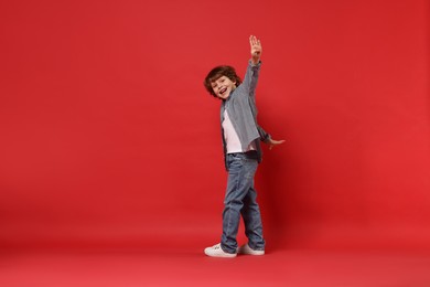 Photo of Happy little boy dancing on red background. Space for text