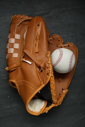 Photo of Catcher's mitt and baseball ball on black slate background, top view. Sports game