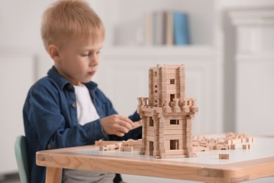 Photo of Cute little boy playing with wooden tower at table indoors, selective focus. Child's toy