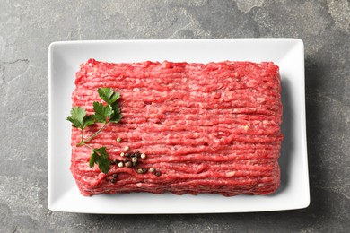 Photo of Raw ground meat, parsley and peppercorns on grey table, top view