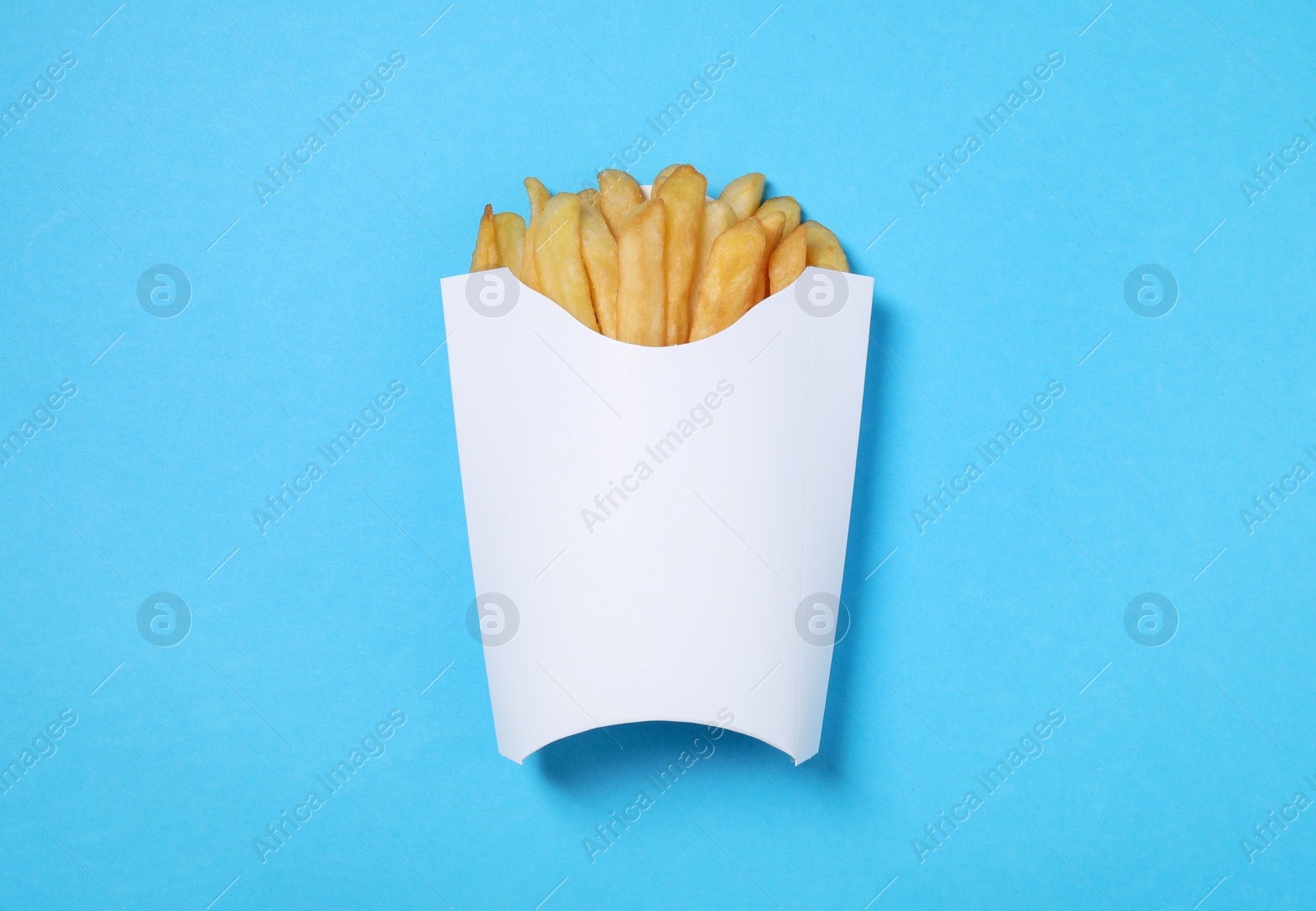 Photo of Paper cup with French fries on light blue table, top view