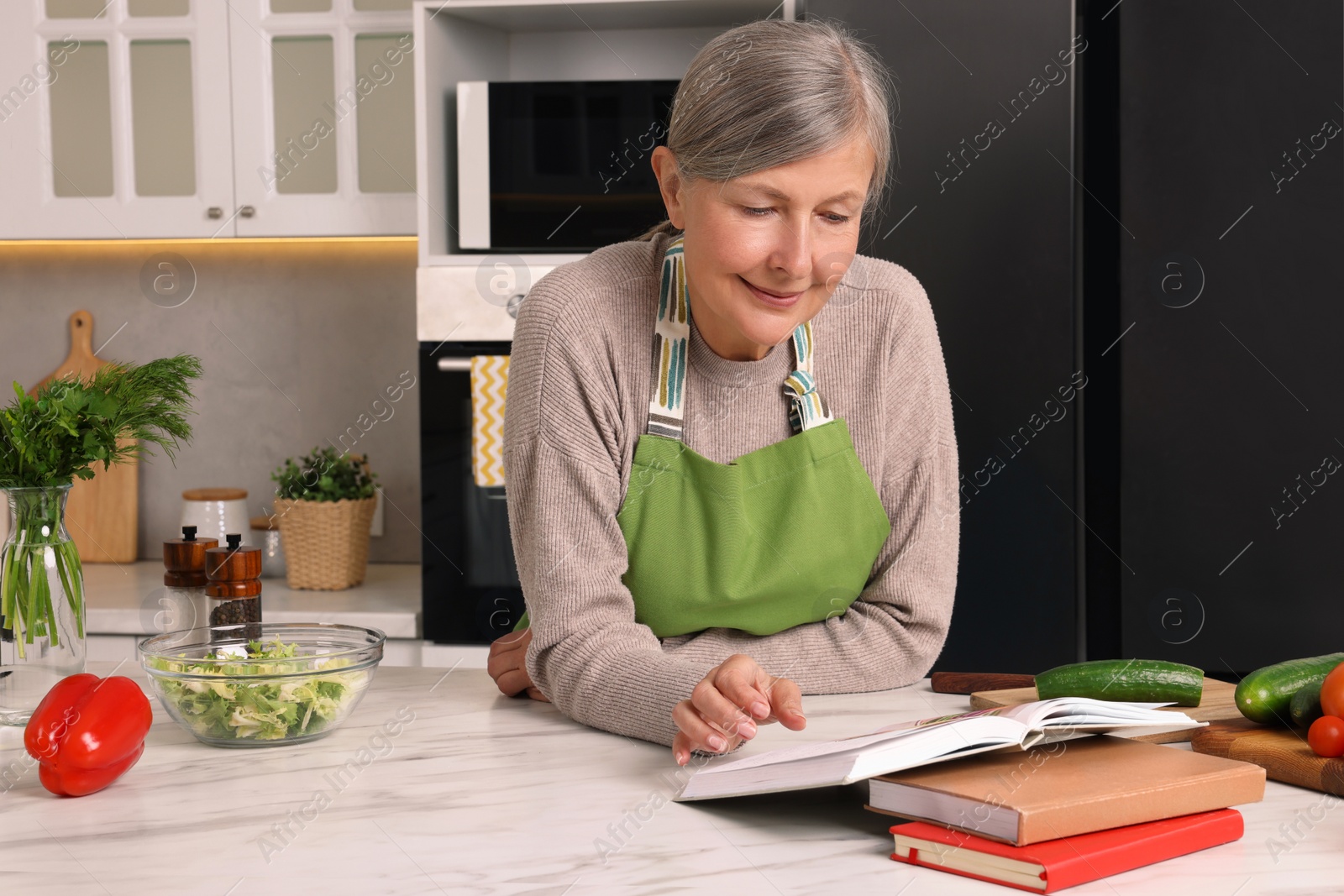 Photo of Happy woman with recipe book at table in kitchen