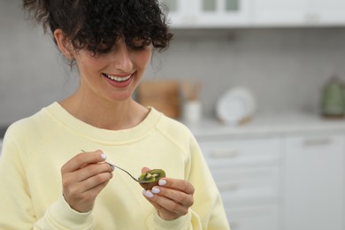 Woman eating kiwi with spoon in kitchen, space for text