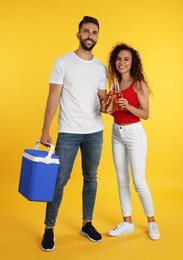 Photo of Happy couple with cool box and bottles of beer on yellow background