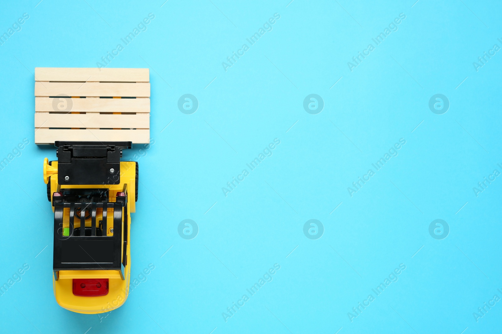 Photo of Toy forklift with wooden pallet on light blue background, top view. Space for text