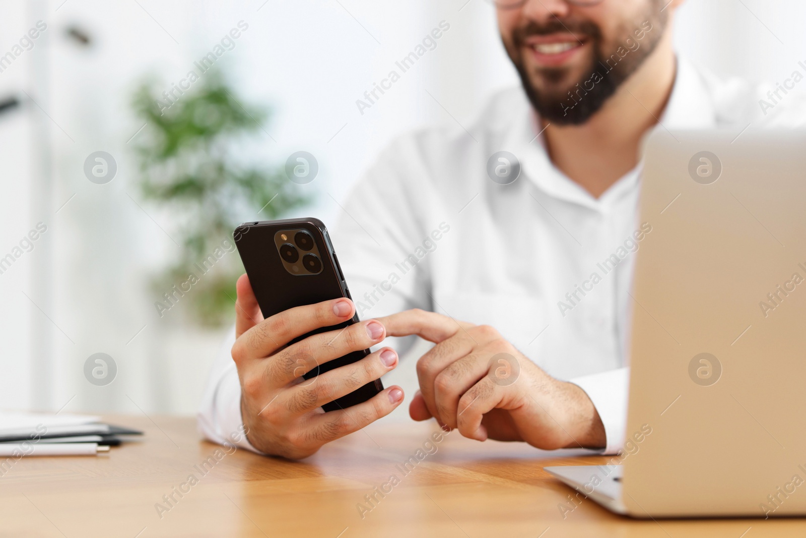 Photo of Young man using smartphone at wooden table in office, closeup