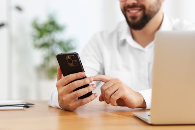 Young man using smartphone at wooden table in office, closeup