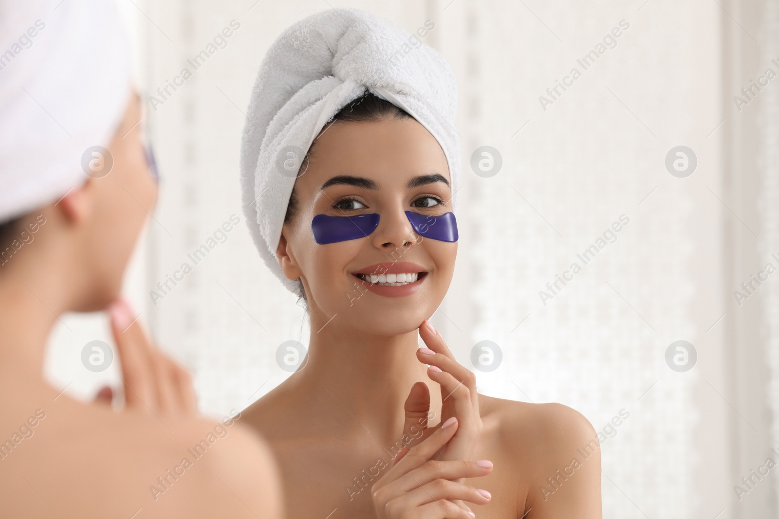 Photo of Beautiful young woman with under eye patches near mirror at home