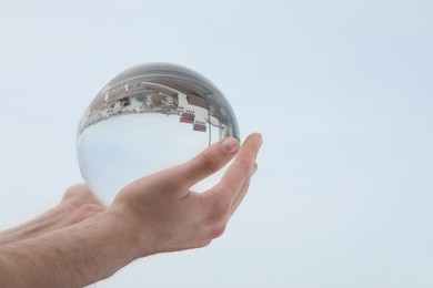 Photo of View of beautiful city street, overturned reflection. Man holding crystal ball against sky, closeup. Space for text