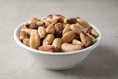 Bowl with tasty Brazil nuts on grey background