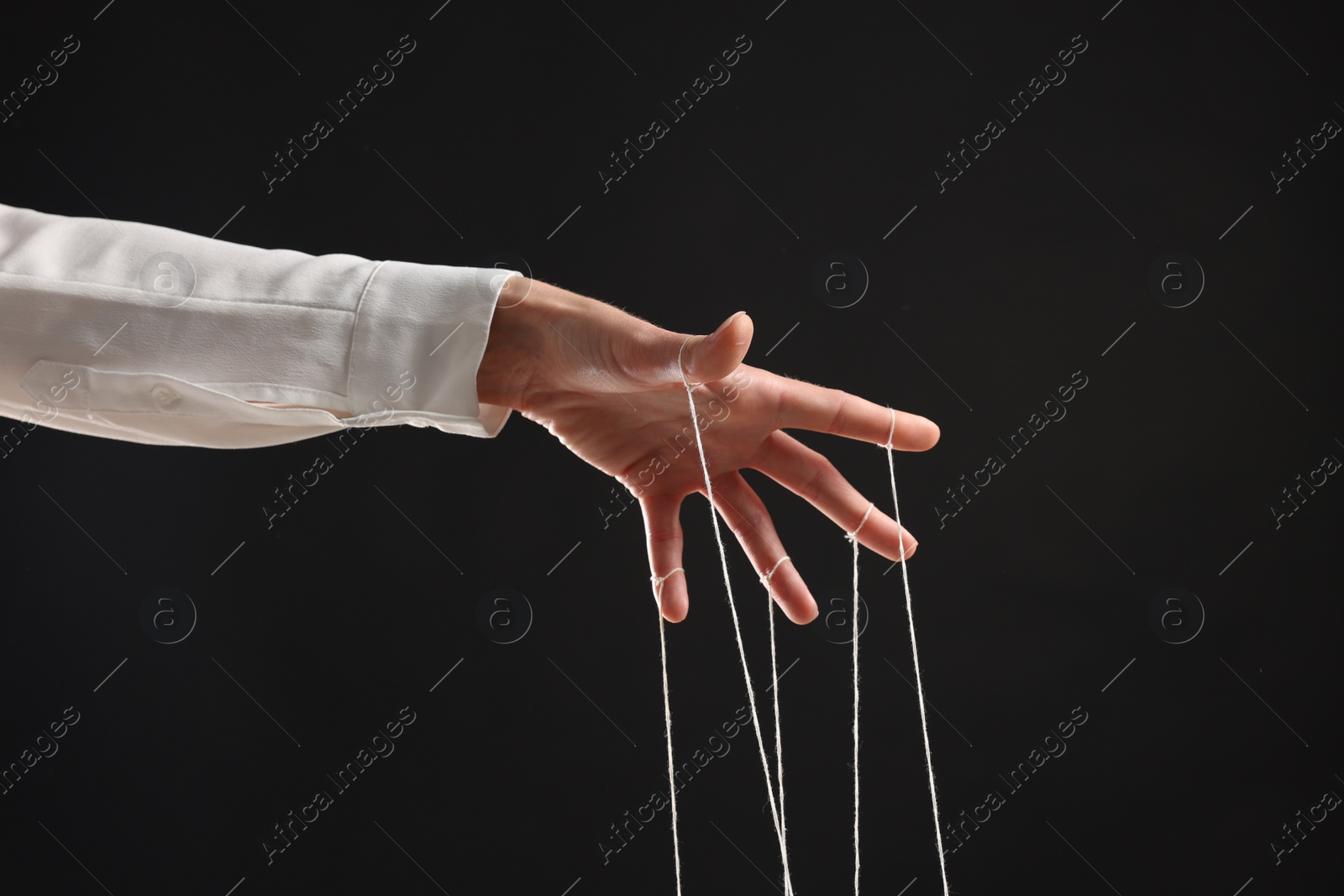 Photo of Woman pulling strings of puppet on black background, closeup