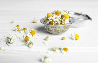 Photo of Dry chamomile flowers in infuser on white wooden table, closeup