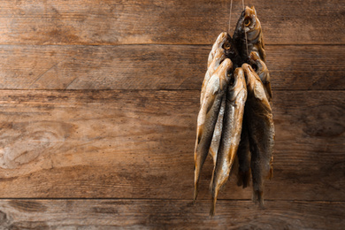 Photo of Dried fish hanging on rope against wooden background, space for text