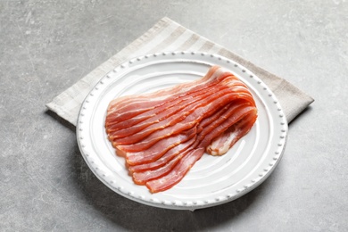 Plate with raw bacon rashers on grey background