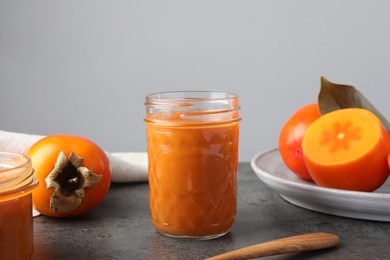 Delicious persimmon jam in glass jar and fresh fruits on gray table
