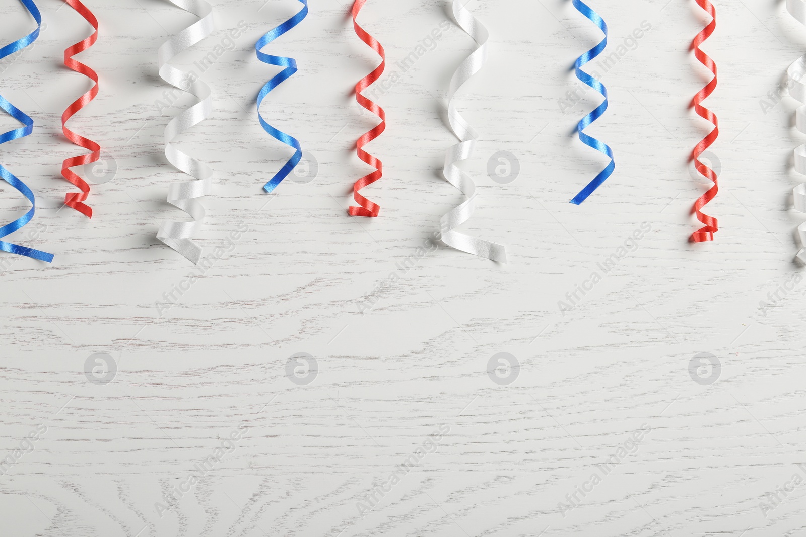Photo of Flat lay composition with colorful party streamers on wooden table, space for text. USA Independence Day