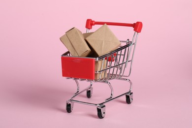 Small metal shopping cart with cardboard boxes on pink background