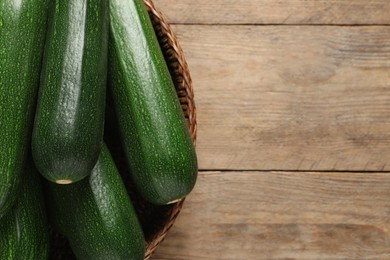 Photo of Raw ripe zucchinis in wicker basket on wooden table, top view. Space for text