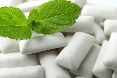 Tasty white chewing gums and mint leaves as background, closeup