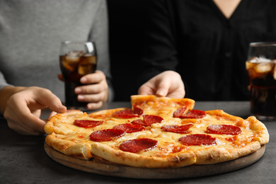 Photo of Women taking tasty pepperoni pizza at grey table, closeup