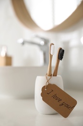 Tag with handwritten text I Love you on toothbrush in bathroom. Romantic message