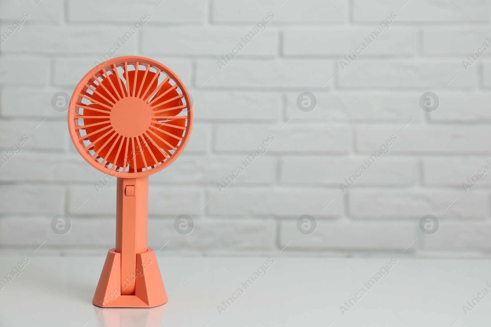 Photo of Portable fan on table near white brick wall, space for text. Summer heat