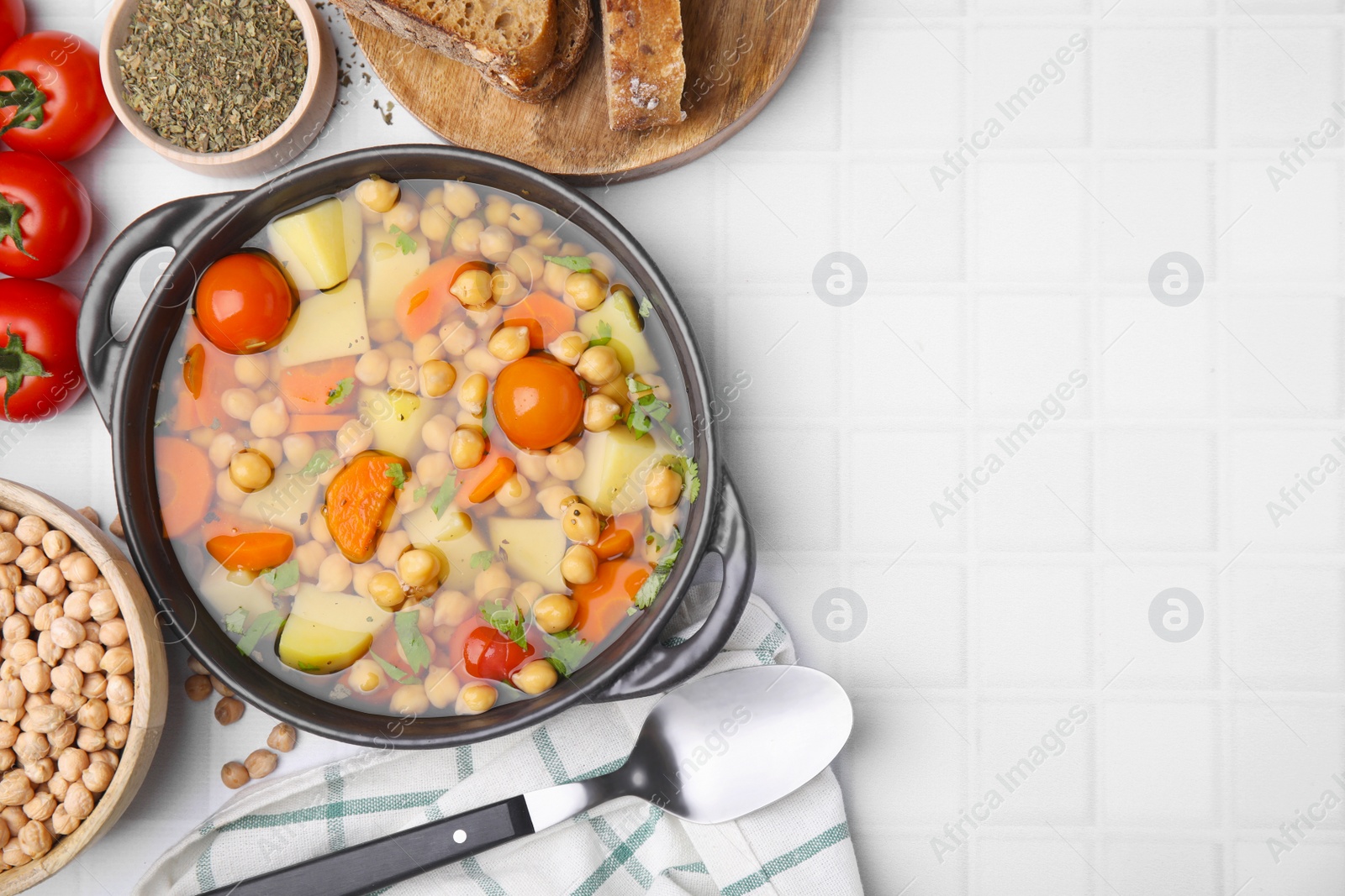 Photo of Flat lay composition of tasty chickpea soup served on white tiled table. Space for text