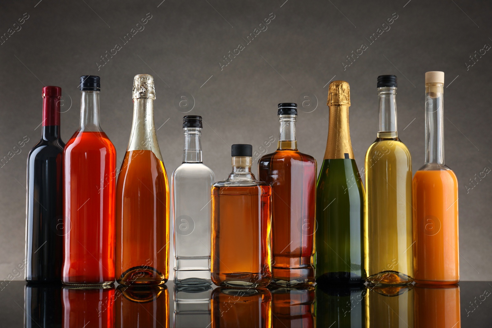 Photo of Bottles of different alcoholic drinks on table against gray background