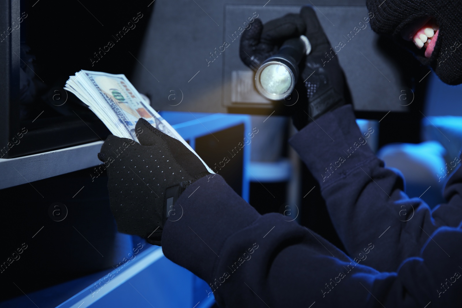 Photo of Thief taking money out of steel safe indoors at night, closeup