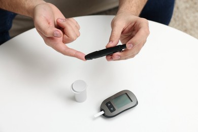 Photo of Diabetes test. Man checking blood sugar level with lancet pen at white table, closeup